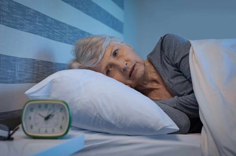 אישה בגיל השלישי לא מצליח להירדם ומסתכל בשעון שמראה על השעה 2 בלילה