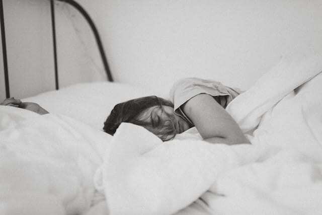 תצלום שחור לבן של אישה ששוכבת במיטה ומכוסה בשמיכה