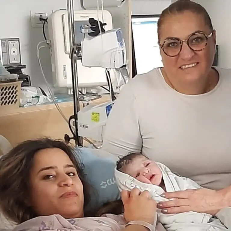 תמונה ובה אביגייל מחזיקה תינוק בחדר לידה ליד יולדת