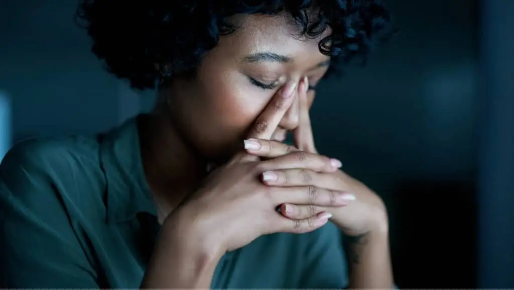 אישה יושבת בחשכה ומחזיק את פניה עם הידיים נראה כסובלת מחרדה, מתח (סטרס)