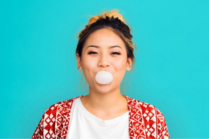 אישה מנפחת בלון מסטיק, צולם על רקע כחול