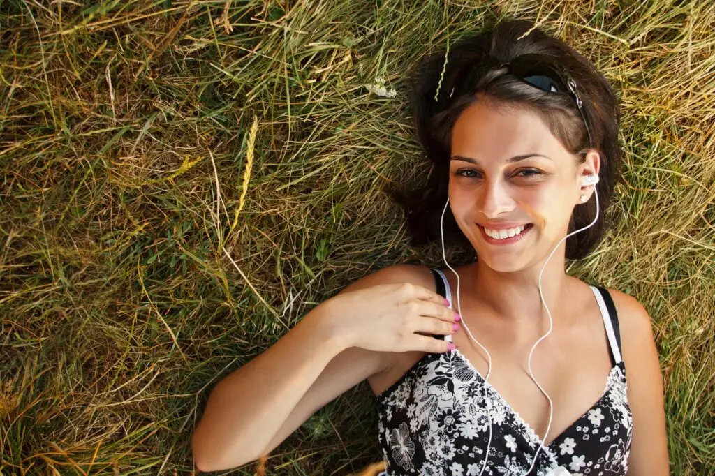 אישה שוכבת על הדשא ושומעת מוזיקה באוזניות