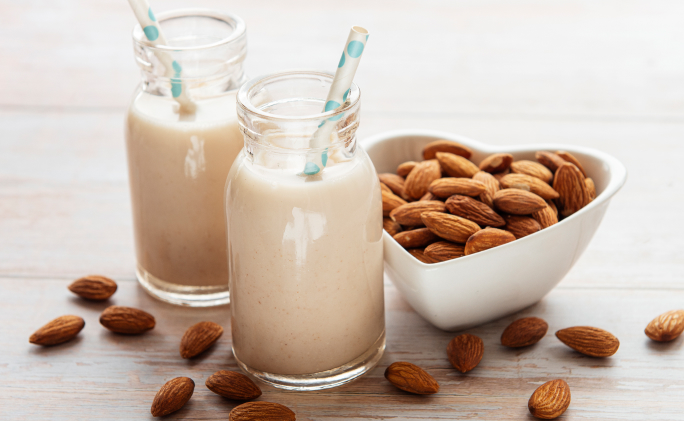 שתי כוסות חלב שקדים עם קש כחול לצד קערת שקדים בצורת לב על רקע לבן