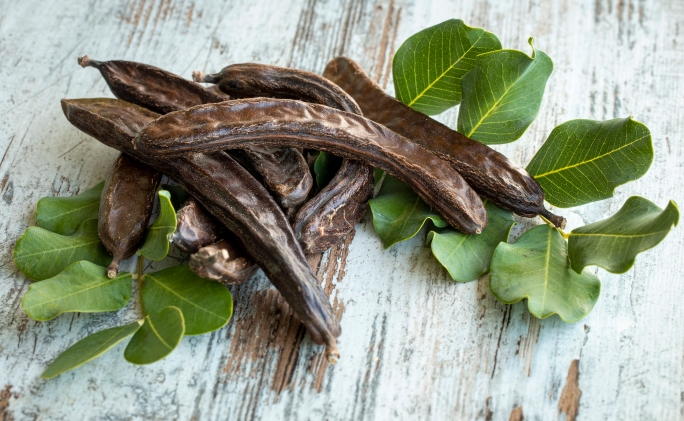 חרובים על שולחן עץ בהיר לצד עלים