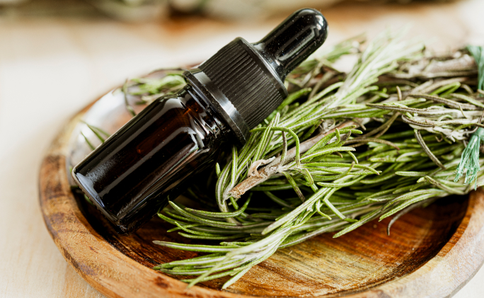 בקבוק ככה של שמן אתרי רוזמרין בתוך כערה עם עלי רוזמרין