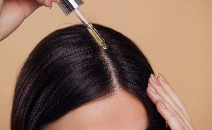 אישה משתמשת בפיפטה עם שמן רוזמרין מהול בשמן נשא על השיער שלה, תצלום תקריב